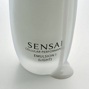 Nahaufnahme der Flasche Cellular Performance Emulsion 1 (Light), wobei das Produkt herabfließt und auf die graue Oberfläche tropft, um die Textur zu verdeutlichen